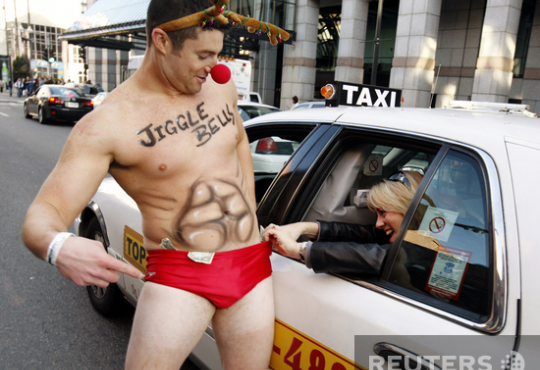 Шон МакЭнти, участник благотворительного Santa Speedo Run в Бостоне, США, собирает пожертвования у пассажиров городского такси