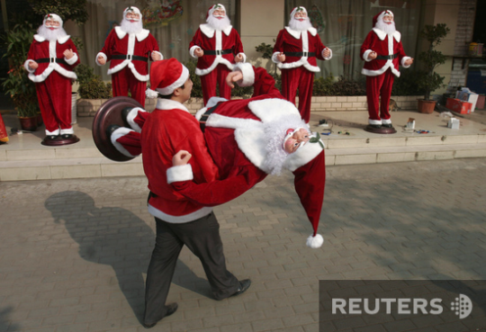 Вухан, Китай. Сотрудник торгового центра устанавливает манекены в костюмах Санта-Клаусов